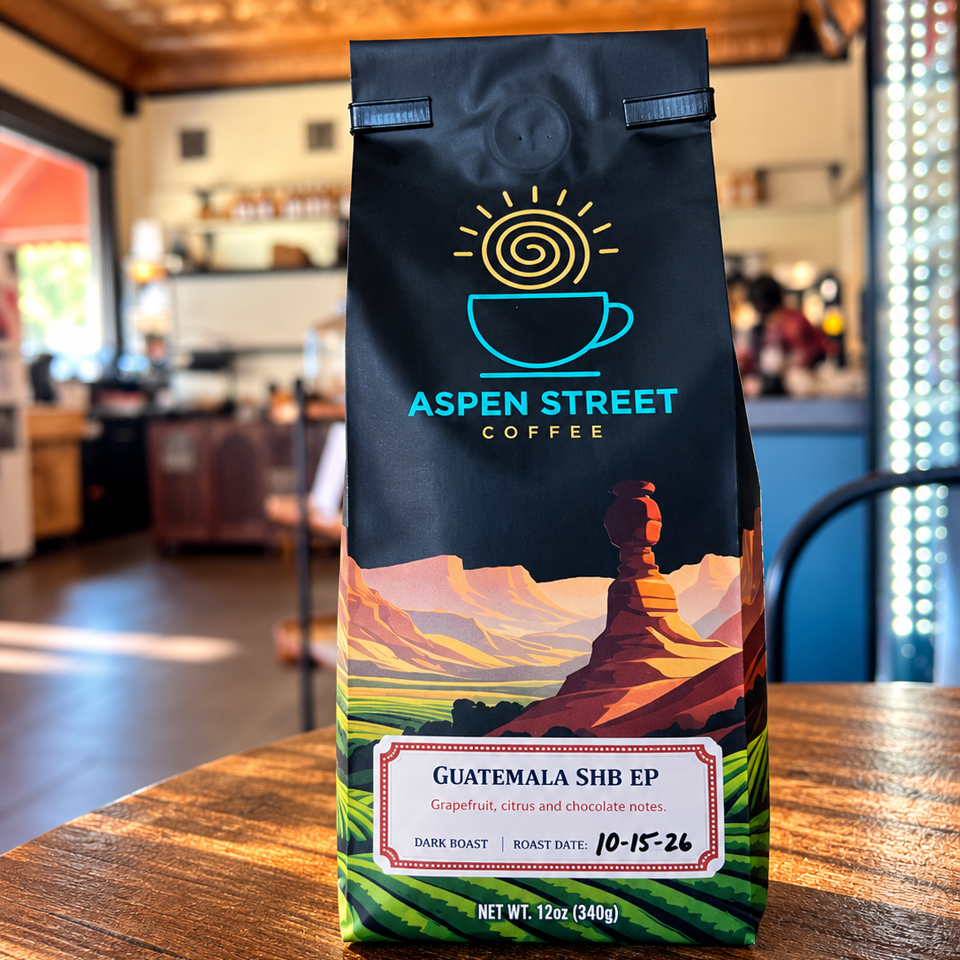 Aspen Street Coffee Guatemala SHB EP dark roast coffee bag displayed on a wooden café table, with mountain artwork and tasting notes.